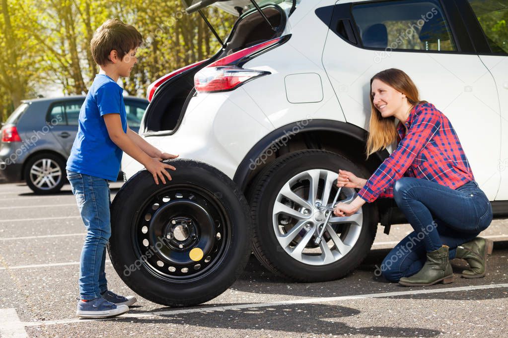 Portrait of little boy rolling donut tire while his mother unscrewing wheel nuts, trying to change flat tyre