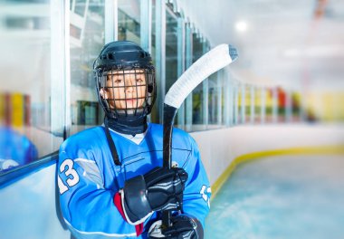 Portrait of young hockey player in protective equipment, standing on ice rink and looking at camera clipart