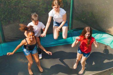 Top view of four friends, teenage girls and boys, bouncing on the outdoor trampoline in summer clipart