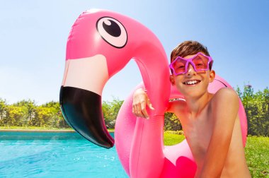 Flamingo şişme halka tutarak ve güneşli gün yüzme havuzu tarafından rahatlatıcı yıldız şekilli güneş gözlüğü takmış genç çocuk portresi