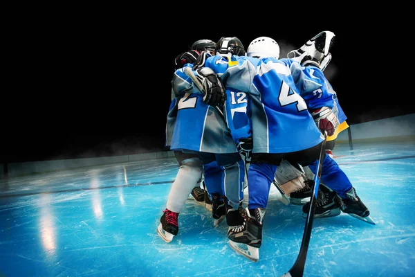 Portrait of children's hockey team standing in circle on ice rink over black background