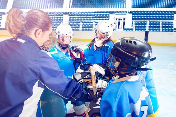 Portrait of female coach and young hockey players joining hands in huddle on ice rink