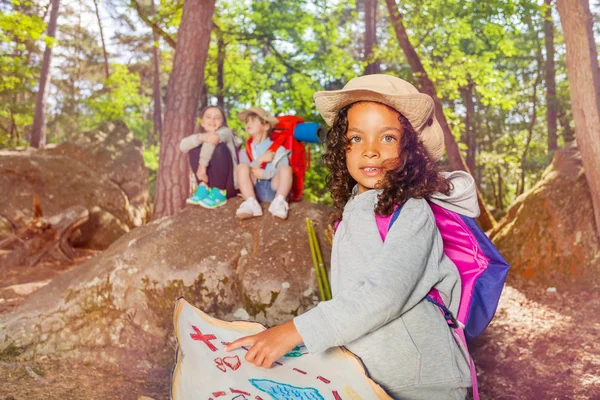 Summer camp game girl with treasure map and other kids in the forest orienting