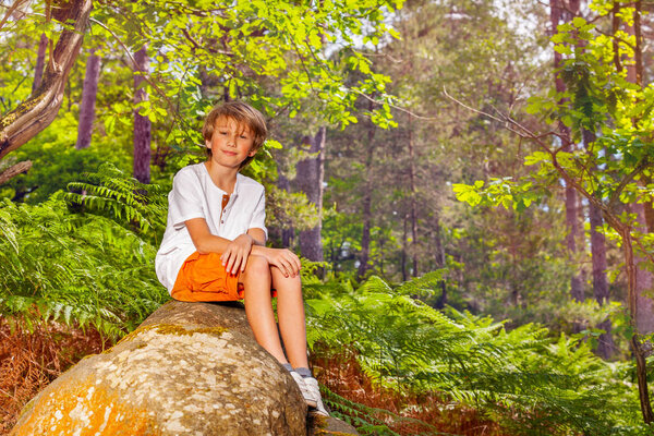 Portrait of school age boy sit on the rock in the forest during hike
