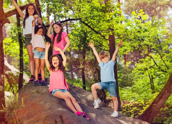 一群孩子坐在岩石上 在远足的休息 欢呼举起双手微笑 — 图库照片