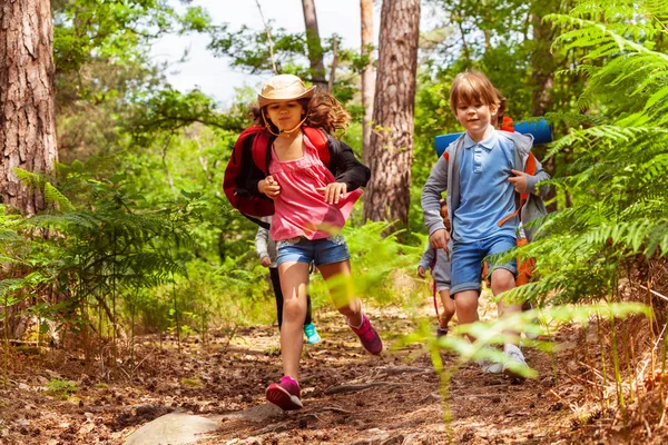 男孩和女孩在小组愉快奔跑快速在森林以微笑穿着休闲衣裳 背包为野营 — 图库照片