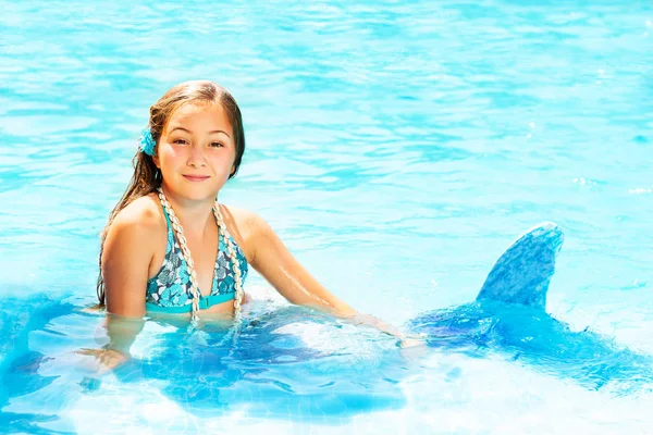 Portrait of beautiful teenage girl in mermaid costume relaxing in blue water of swimming pool