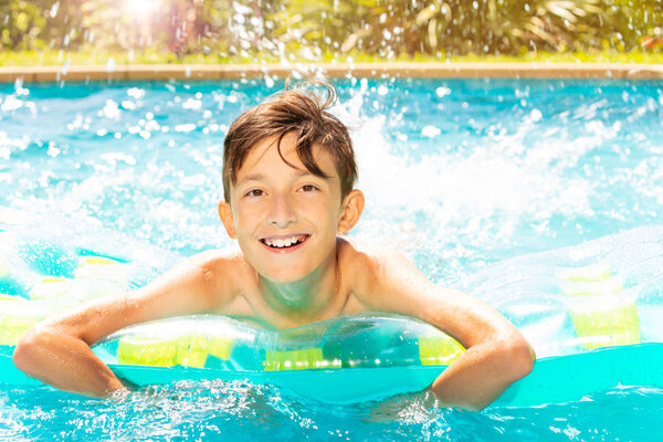 Close-up portrait of teenage boy swimming on air mattress and splashing water in outdoor pool