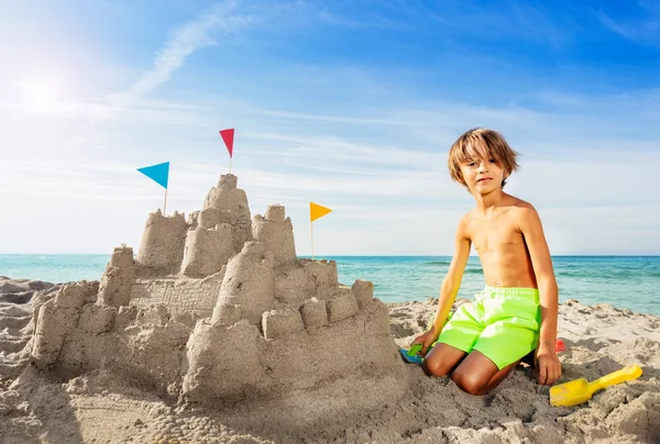 ビーチに座っていると 夏に大きな砂の城を構築幸せな少年の肖像画 — ストック写真