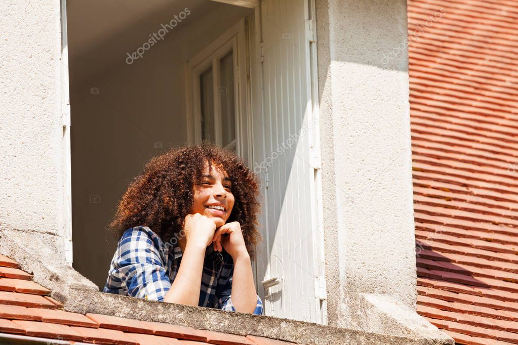 Portrait of happy African girl teenager admiring the landscape from the attic floor window