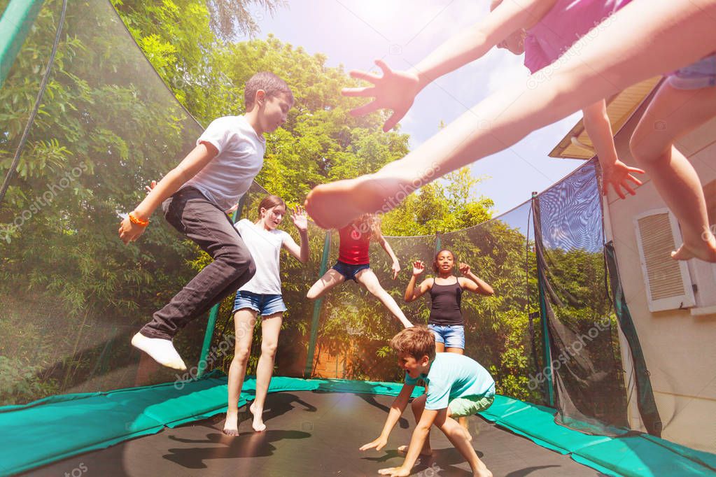 Big group of age-diverse boys and girls playing on the outdoor trampoline in summer