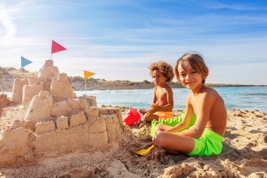 Portrait of two happy boys building big sand castle on the beach clipart