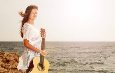 Gitar holding, sahilde duran ve kameraya bakıyor güzel genç kız portresi