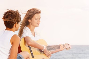 Güzel kız gitar çalmak ve sahilde şarkı dinleme genç çocuk portresi
