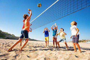 Genç erkek ve kız sahilde voleybol oynarken büyük grup