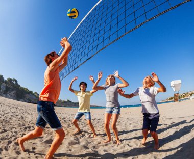Teenage boy jumping to spike volleyball over net while his opponents defending the pole clipart