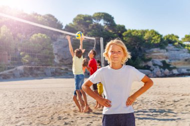 Plaj voleybolu arkadaşlarıyla oynarken gülümseyen genç çocuk portresi