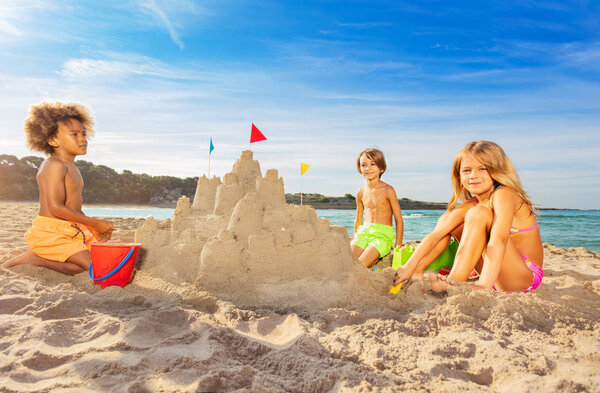 Portrait of happy kids, multiethnic boys and girls, building big sand castle on the beach