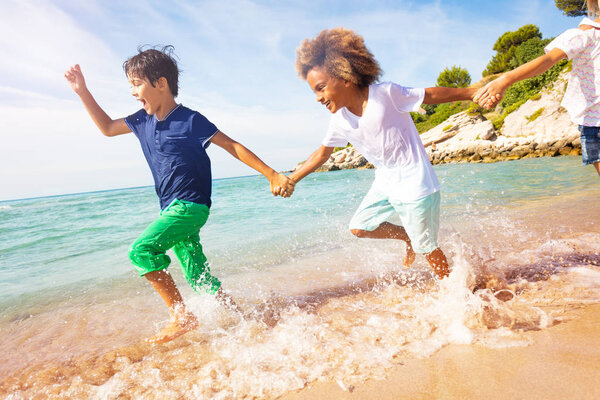 Portrait of happy boys holding hands and running in shallow water on the beach