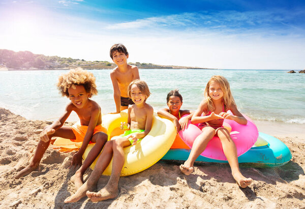 Big group of multiethnic kids, happy boys and girls, sitting on inflatable mattresses at the seaside