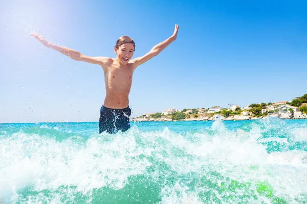 浅水波のジャンプ 彼の手を上げるとカメラを見て幸せな 代の少年の肖像画 — ストック写真