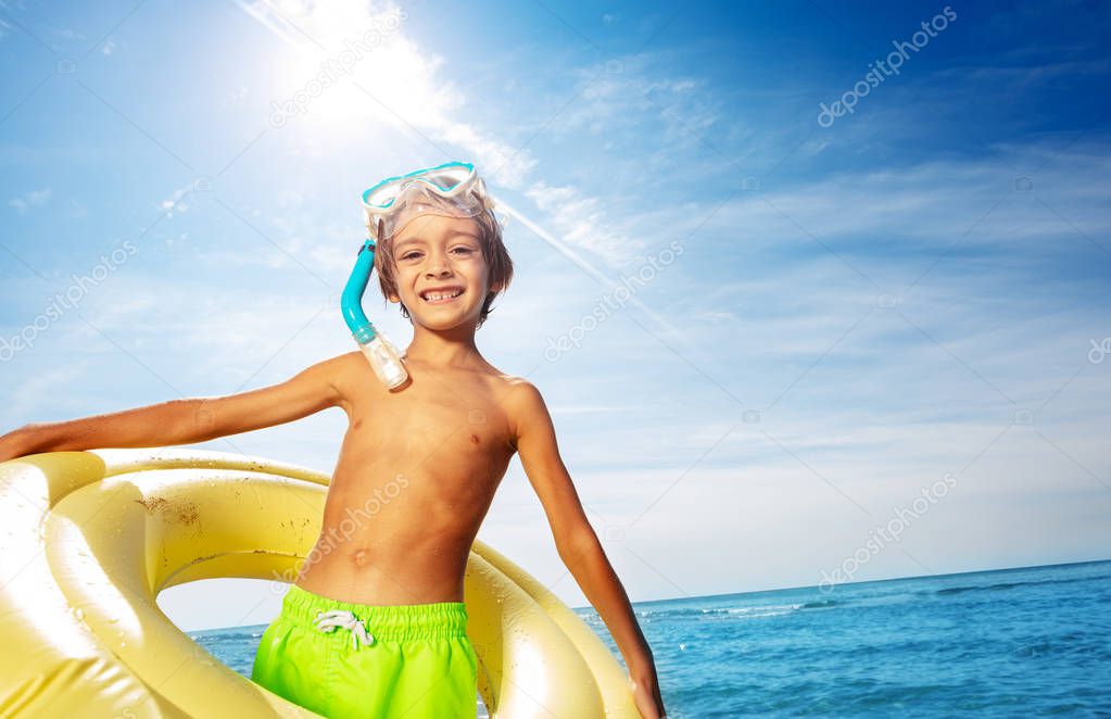 Portrait of happy boy with scuba mask and big swimming ring against tropical seascape