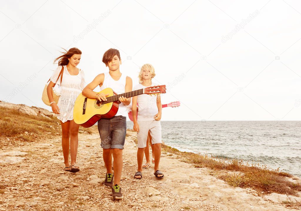 Teenage boy walking on the beach with friends and playing guitar