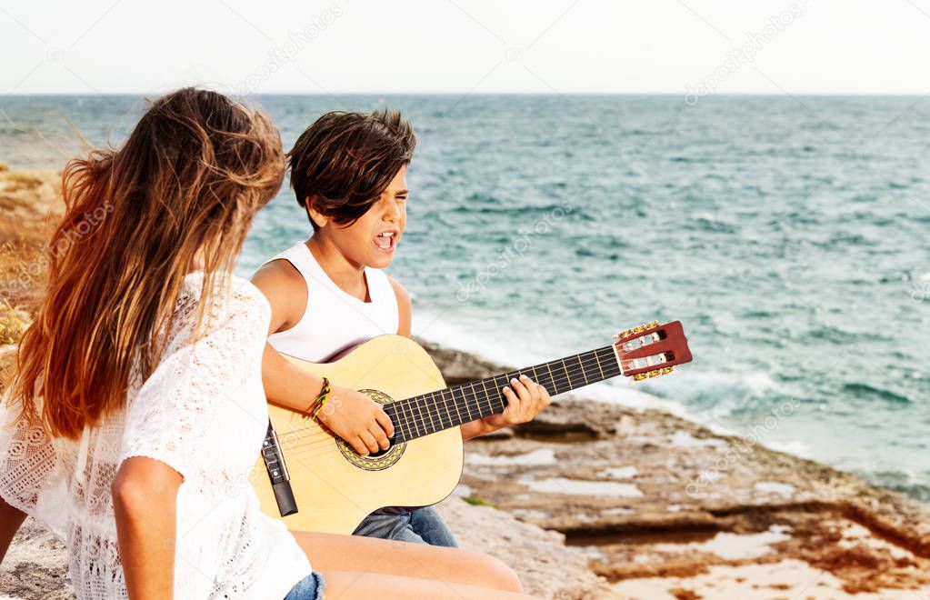 Portrait of teenage boy playing guitar and singing romantic song for beautiful girl at the seaside