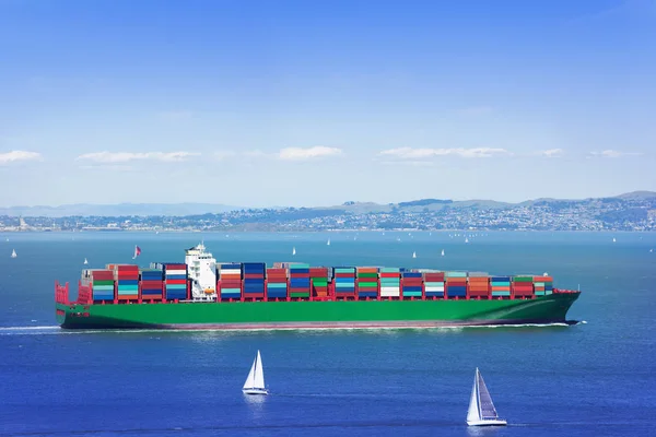 青い空と白いヨットの中で海の完全ロードされた貨物船 — ストック写真