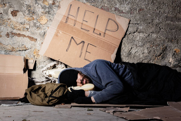 Beggar in tattered clothes sleeping at sidewalk