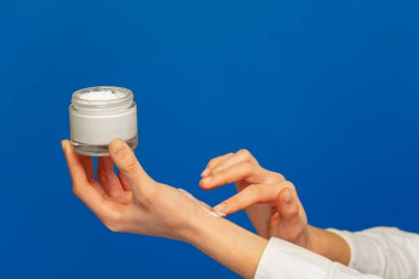 Eline kozmetik krem uygulayan kadın, mavi arka plan üzerinde izole