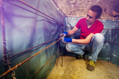 Beton dökümü için bodrum çerçeve inşa eden pliers metal çubuklar ile bir adam elleri tel portresi