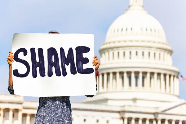 Woman protest in front of the USA capitol in Washington holding sign saying shame