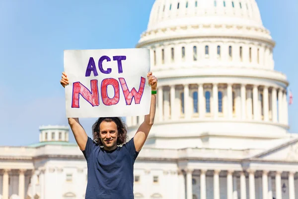 Man protest in front of the USA capitol in Washington holding sign saying act now in his hands