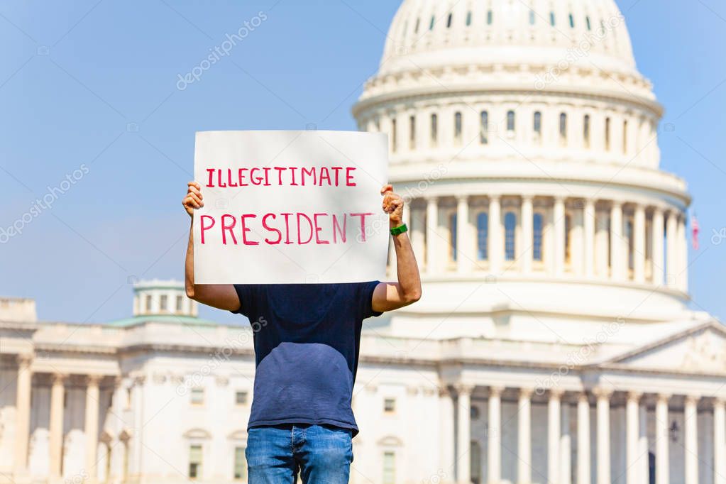 Man protest in front of the USA capitol in Washington holding sign sayin  illegitimate president