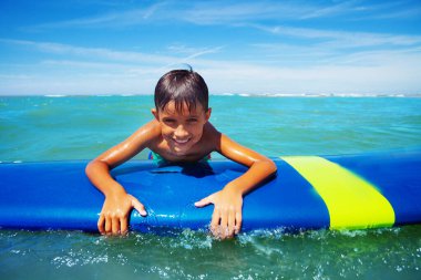 Sörf tahtasında gülümseyen küçük bir sörfçü çocuğun portresi.