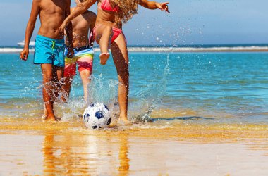 Çocuklar sahilde futbol oynarlar, su kenarında futbol toplarını yumruklarlar, deniz dalgalarında su sıçratırlar, yakın çekim yaparlar.