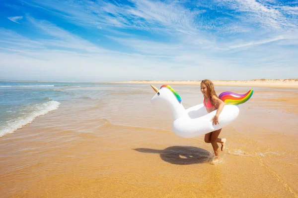 美しいです笑顔の女の子へザ波で泳ぐインフレータブルユニコーンオンザ砂の海のビーチ — ストック写真