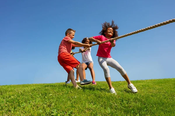 Group of kids pull rope with passion and emotion over blue sky in park