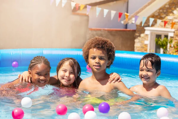 4人の幸せな子供たちのグループ女の子と男の子遊びます座って抱擁でプールで熱い夏の日持ち上げ手アップ笑顔 — ストック写真