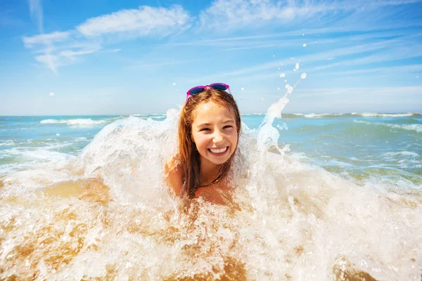 幸せな小さな美しい女の子は波が彼をカバーし ビーチの山の上に横たわり 大きなかわいい笑顔を表現 — ストック写真