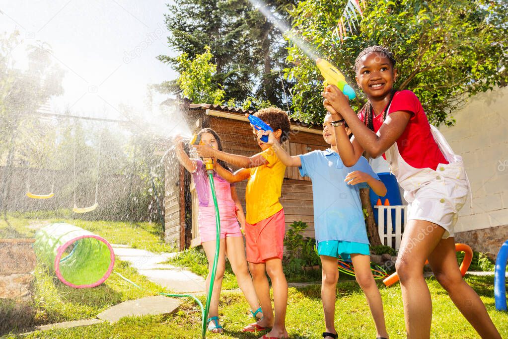 Boys with girls in the middle of water gun fight shooting guns, pistols and garden hose sprinkler