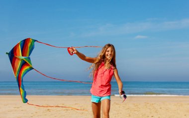 Güzel bir kızın portresi koşuyor ve deniz arka planında renkli soyulmuş uçurtmayla oynuyor.