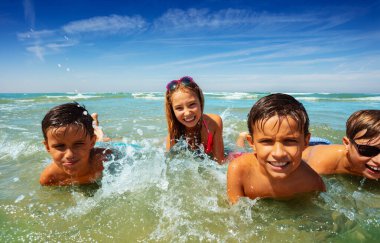 Bir grup küçük çocuk birlikte deniz dalgalarında yatıp oynuyorlar.