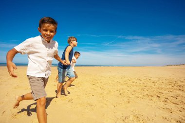 Sahilde eğlenmek. Bir grup kız ve erkek, deniz kenarında kumların üzerinde el ele koşuyorlar.