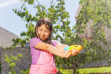 Diğer çocukların ateşi altında ıslak bir kızla duygusal aktif su savaşı oyunu.