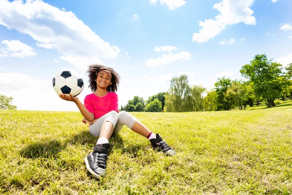 少し可愛いです巻き黒美しいです女の子ホールドサッカーボールで片手座っていますザ草 — ストック写真