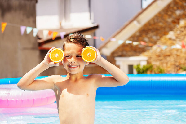 Nice happy little boy holding oranges close to the head and making fun playing in the pool