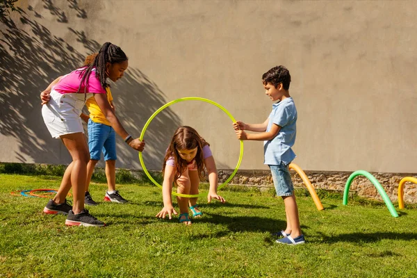 Group of friends play with color sport hoops, little long hair girl jumps inside hold by two kids