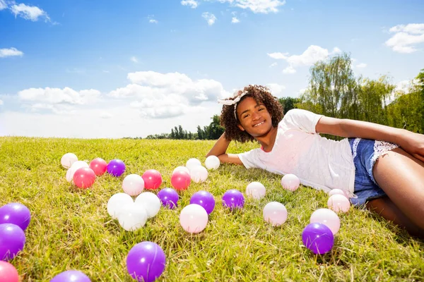 漂亮的黑卷曲姑娘 长着五彩缤纷的球躺在草地上 — 图库照片